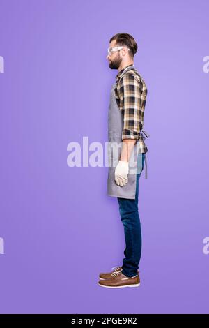 Bottoncino per il corpo di dimensioni normali, vista laterale metà faccia ritratto di carpentiere seducente e calmo con acconciatura in occhiali di sicurezza, jeans, sfondo grigio isolato Foto Stock