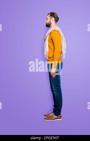 Full size fullbody snap, vista laterale metà faccia ritratto di bel stilista attraente in maglione, jeans con sciarpa intorno al collo isolato sul grigio Foto Stock
