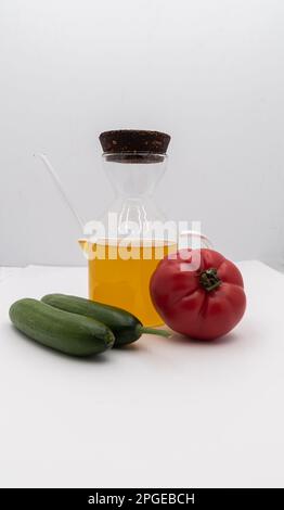 Concetto di cibo sano. Olio d'oliva in bottiglia di vetro e pomodoro e cetrioli su fondo bianco isolato. Foto Stock