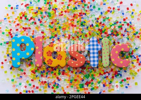 Cumulo di granuli multicolore di resina plastica su sfondo bianco con lettere in caratteri plastica Foto Stock