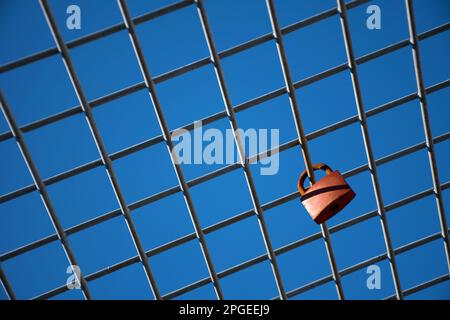 Lucchetto rosso contro il cielo blu sulla griglia metallica Foto Stock