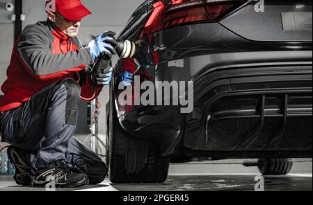 Addetto al dettaglio dell'auto rimuovere l'acqua dalla carrozzeria dell'auto utilizzando un panno morbido. Preparazione per una cera. Vista posteriore del veicolo moderno. Foto Stock