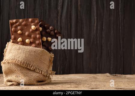 Cioccolato al latte e nero con gocce di cioccolato in un sacchetto su un vecchio sfondo di legno con spazio per il testo. Illustrazione concettuale del cioccolato fatto a mano Foto Stock