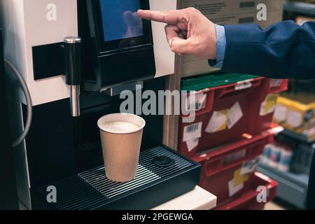 vista ritagliata di un uomo d'affari che preme il pulsante sulla macchina per il caffè mentre prepara il caffè. Un uomo acquista il caffè da una macchina da caffè. Foto Stock