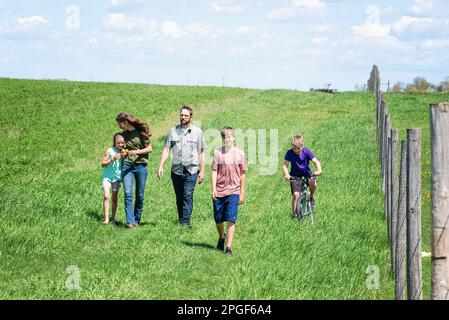 Famiglia di cinque persone che camminano in un campo del paese. Foto Stock