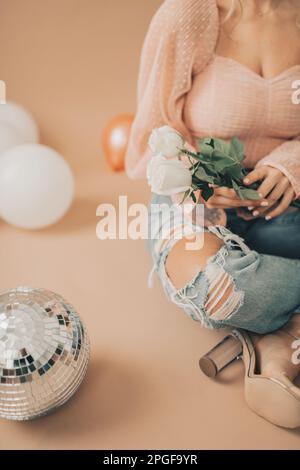 Primo piano della donna seduta che tiene rose bianche vicino alla palla da discoteca Foto Stock