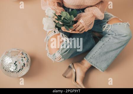 Primo piano della donna seduta che tiene rose bianche vicino alla palla da discoteca Foto Stock