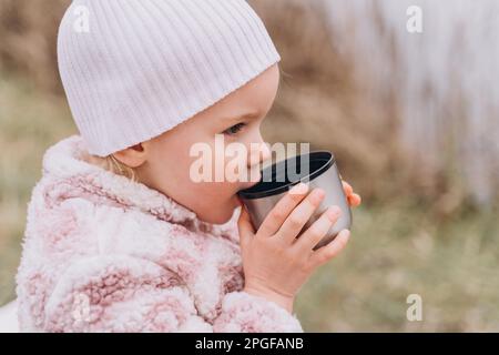 Bambina in abiti caldi rosa chiaro beve il tè da un thermos Foto Stock