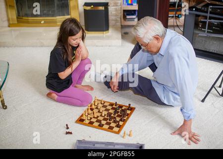 Una bambina si siede sul pavimento con il nonno che gioca a scacchi Foto Stock