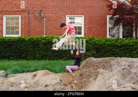 Una ragazza con il telefono filma fratello saltando sopra la testa in un'abisso Foto Stock