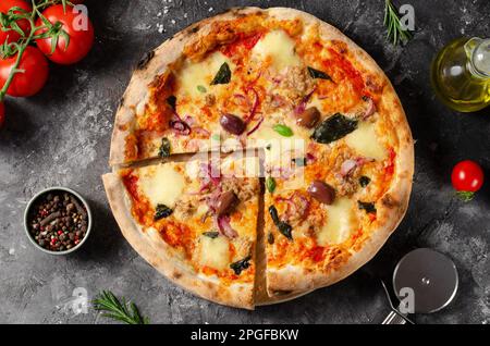 Pizza al tonno, pizza appena sfornata con tonno, mozzarella, cipolla, basilico e olive su sfondo rustico scuro Foto Stock