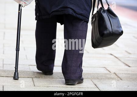 Donna anziana che cammina con la canna su una strada, le gambe sul marciapiede. Concetto di disabilità, adulta anziana limping, malattie della colonna vertebrale Foto Stock