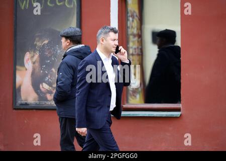 Uomo in tuta da lavoro che parla sullo smartphone mentre cammina per strada. Uso del telefono cellulare in città Foto Stock