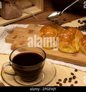 Colazione uruguayana. Croissant con gelatina. Cucchiaio con tazza Pull con caffè appena servito. Ancora vita Foto Stock