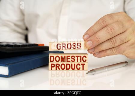 Concetto aziendale. Nelle mani di un uomo d'affari, blocchi di legno con l'iscrizione - PRODOTTO INTERNO LORDO, accanto a un notebook e una calcolatrice. Foto Stock