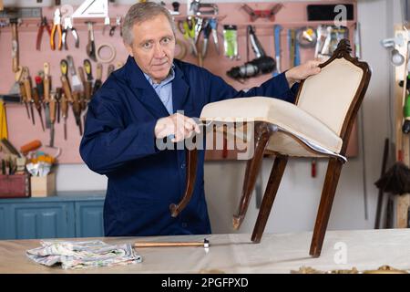 Vecchio produttore di mobili maschi che lavora su sedia vintage in officina Foto Stock