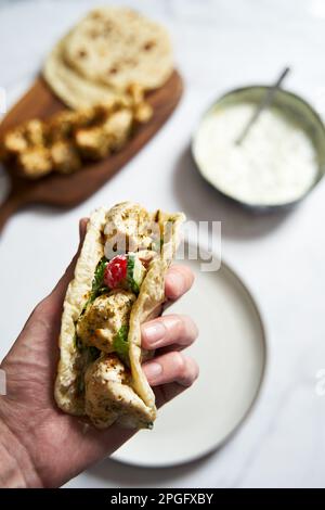 Souvlaki ona pita di pollo greco con verdure fresche e salsa tzatziki. Mano che tiene una pita con souvlaki di pollo. Sullo sfondo c'è un pollo Foto Stock