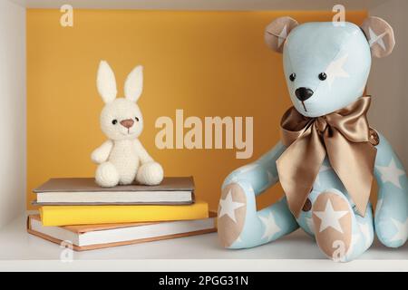 Orso giocattolo e coniglietto con libri sullo scaffale vicino alla parete gialla Foto Stock