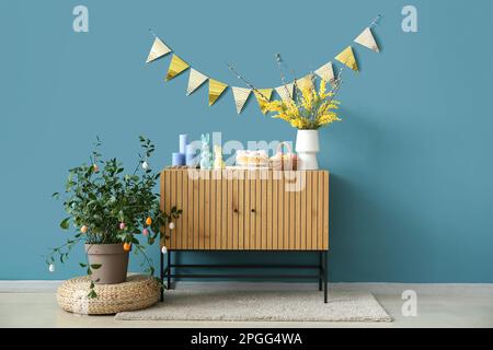 Decorazioni pasquali su armadio in legno vicino alle pareti blu Foto Stock