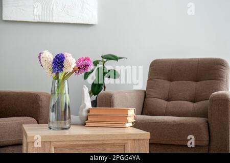 Vaso con bellissimi fiori giacinto, libri e ceramica mano sul tavolo da caffè in soggiorno Foto Stock
