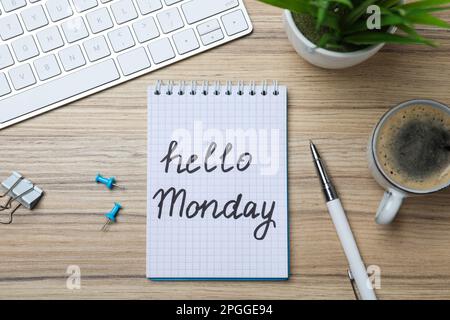Messaggio Ciao Lunedi scritto in notebook, tastiera del computer e tazza di caffè su scrivania di legno, piatto Foto Stock