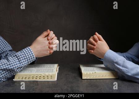 Coppia che prega sulle Bibbie a tavola grigia, primo piano Foto Stock