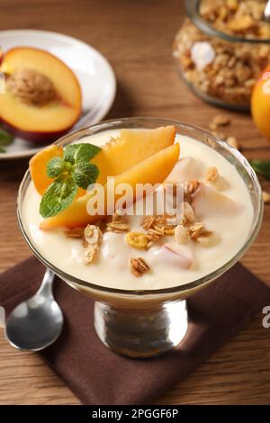 Gustoso yogurt alla pesca con muesli, menta e frutta in ciotola da dessert su tavolo di legno Foto Stock