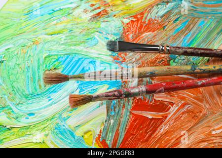 Vista in primo piano della tavolozza dell'artista con colori e pennelli misti come sfondo Foto Stock