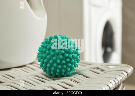 Palla asciugatore turchese e detersivo per bucato su cesto di vimini vicino alla lavatrice, primo piano Foto Stock