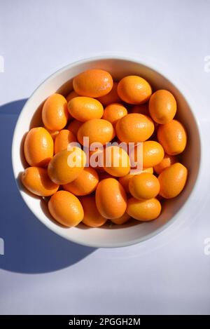 Ciotola bianca piena di piccoli kumquat, al sole Foto Stock