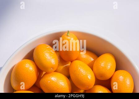 Ciotola bianca piena di piccoli kumquat, al sole Foto Stock