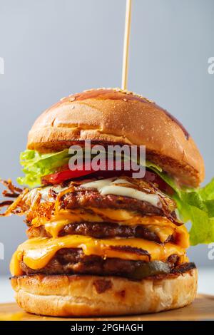 Cheeseburgers caricato tre polpette triplicate impilate alte con strati di formaggio, lattuga e pomodoro. Cheeseburger alto Foto Stock