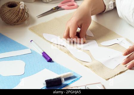 Mani femminili tagliate che prendono le misure e pinning i modelli di cucitura della carta ad un foglio tessile sul tavolo. Filo ricamato e lavorazione ad ago Foto Stock