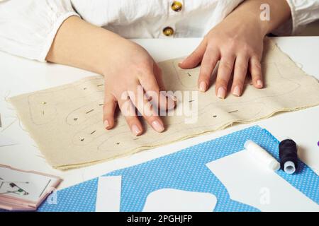 Donna corto seamstress mani che si aggraffano e facendo cucire disegni creativi su foglio di tessuto su tavolo. Lavorazione ad ago, processo di cucitura del filo. Cucire Foto Stock