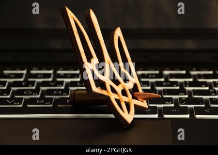 Una pallottola e uno stemma di legno dell'Ucraina giacciono su una tastiera nera del notebook Foto Stock