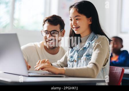 Insegnante che aiuta una giovane ragazza a capire una lezione di alfabetizzazione digitale in una classe. Utilizzando un computer portatile, l'educatore guida lo studente attraverso il computer Foto Stock