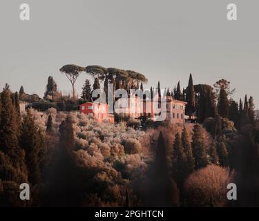 Una casa a due piani arroccata sulla cima di una collina, circondata da lussureggianti alberi verdi in primo piano Foto Stock