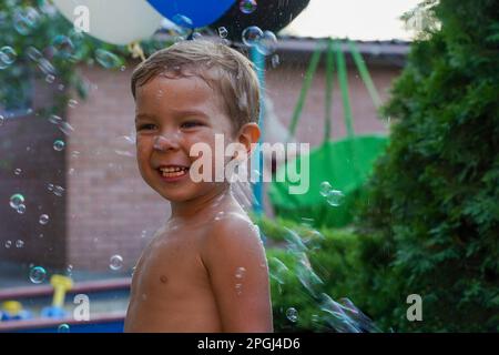 Un ragazzino in un flusso di bolle di sapone. Una frothy festa di compleanno nella natura. Messa a fuoco morbida Foto Stock