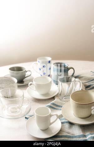 Diverse tazze vuote di caffè e tè su un tavolo rotondo con un asciugamano da cucina azzurro contro una parete beige con spazio copia, fuoco selezionato, nar Foto Stock