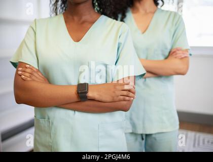 Primo piano corto di due operatori sanitari che indossano scrub con le braccia piegate Foto Stock