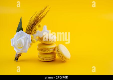 semplice fiore bottone foro appoggiato su una pila di macaroon matrimonio favori isolati su uno sfondo giallo Foto Stock