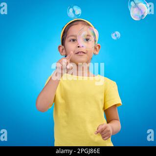 Bambini, carino e una ragazza che schioccano le bolle su uno sfondo blu in studio per divertimento o sviluppo del bambino. Ragazzi, abilità motorie e puntare con una donna Foto Stock