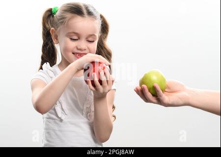 La bambina sceglie fra due mele, mela rossa o verde, scelta del bambino, sfondo bianco e spazio della copia. Foto Stock