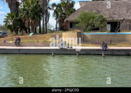 Tre persone si siedono lungo il fiume Rio grande sul lato messicano del fiume, confine tra Stati Uniti e Messico. Foto Stock