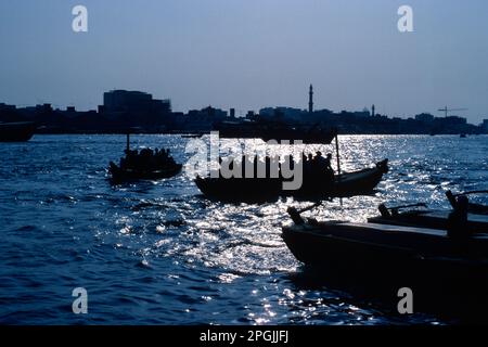 Dubai UAE 1976 – silhouette di taxi acquei abra sul torrente che viaggiano tra i quartieri di Bur Dubai e Deira di Dubai negli Emirati Arabi Uniti Foto Stock