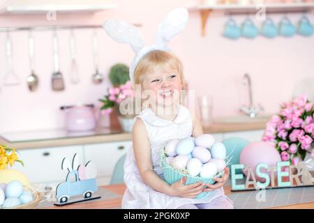 Carina bambina con orecchie coniglietto tenendo uovo di Pasqua in cucina decorata per Pasqua Foto Stock