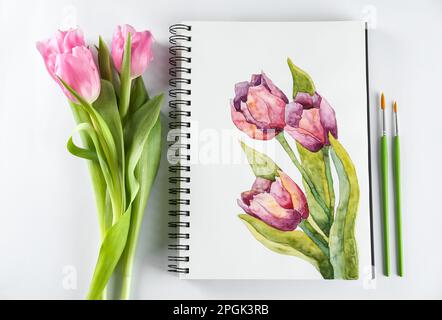 Pittura tulipani in quaderno, fiori e pennelli su fondo bianco, giacitura piatta Foto Stock
