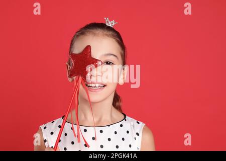 Ragazza carina con corona piccola e bacchetta magica su sfondo rosso. Piccola principessa Foto Stock