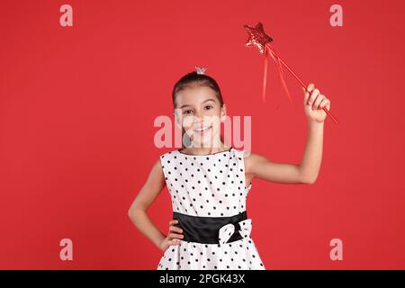 Ragazza carina con corona piccola e bacchetta magica su sfondo rosso. Piccola principessa Foto Stock