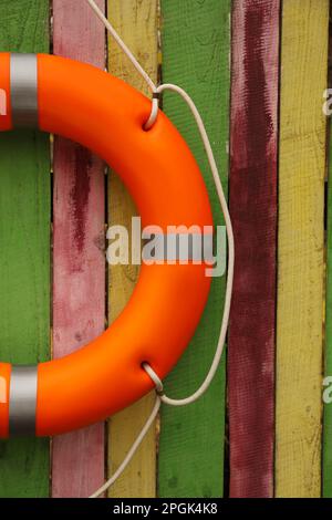 Salvagente arancione appeso a una recinzione di legno colorata. Attrezzatura di salvataggio Foto Stock